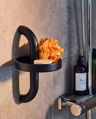 Portavelas negro de pared con asa curvada que sostiene una flor seca naranja. Botella oscura visible al fondo