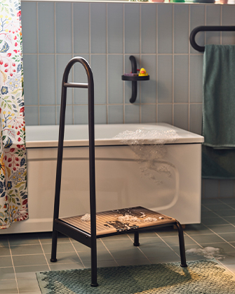 Taburete negro con estante de almacenaje junto a bañera en baño con azulejos