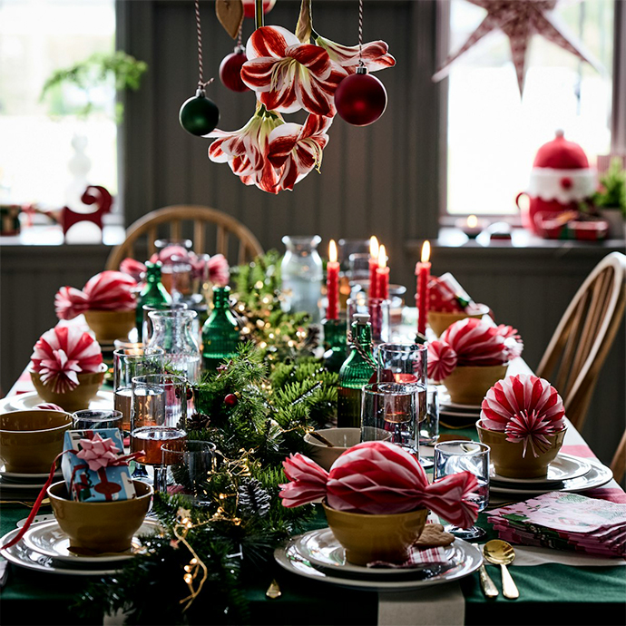 Mesa de cena navideña con decoraciones rojas y blancas, centro de mesa de pino, velas encendidas y vajilla para celebrar las fiestas