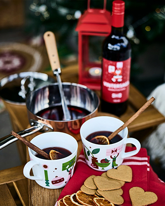 Dos tazas navideñas con vino caliente junto a una cacerola y botella de vino. Ideal para entrar en calor durante las noches frías de invierno