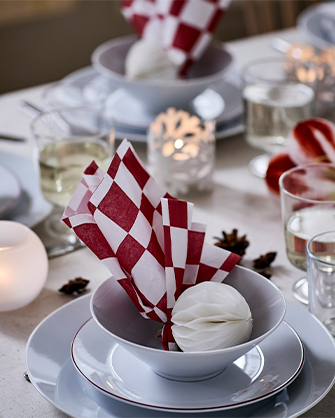 Mesa puesta con platos blancos, servilletas a cuadros rojos y blancos, y velas que crean un ambiente acogedor para comer