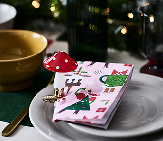 Servilletas navideñas con patrón de árboles festivos sobre plato blanco junto a taza dorada en mesa decorada para las fiestas