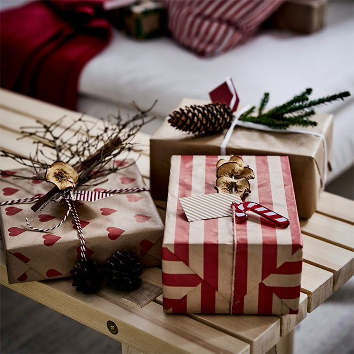 Wrapped Christmas gifts on wooden tray with natural decorations. Brown paper, red striped wrapping, pine cones and evergreen branches create festive display