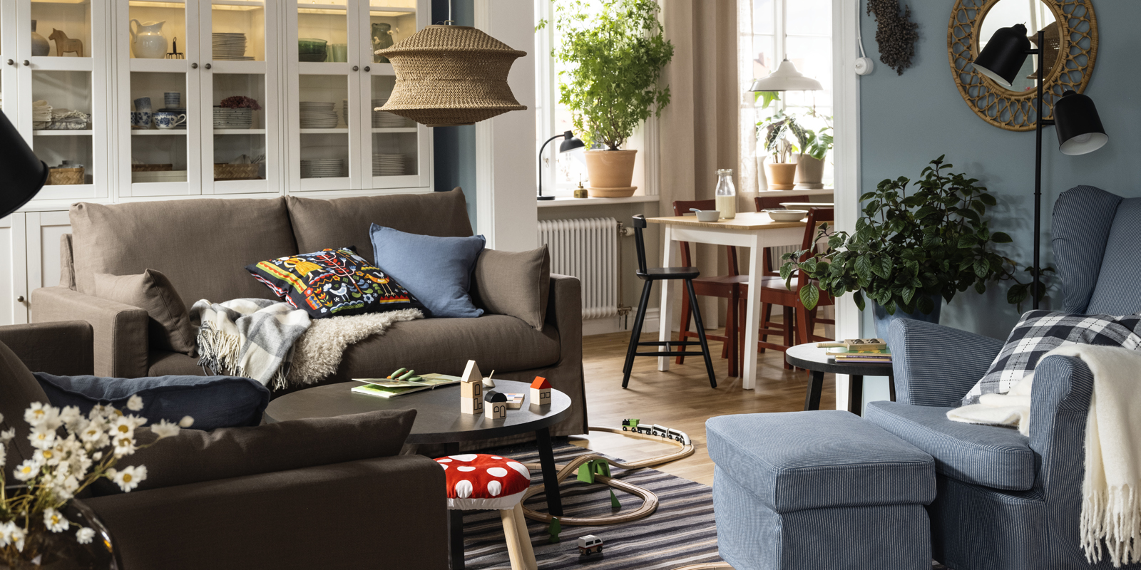 Two HYLTARP sofas stand opposite a STRANDMON wing chair and footstool on a woollen RÅVAROR rug in a exible living room.