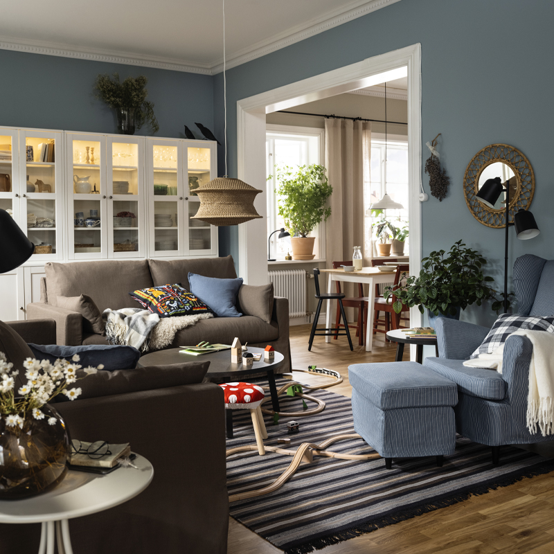 Two HYLTARP sofas stand opposite a STRANDMON wing chair and footstool on a woollen RÅVAROR rug in a exible living room.