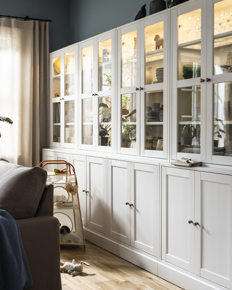 Some white HAVSTA storage combinations with glassdoors stand against a wall behind a grey-brown HYLTARP sofa-bed.