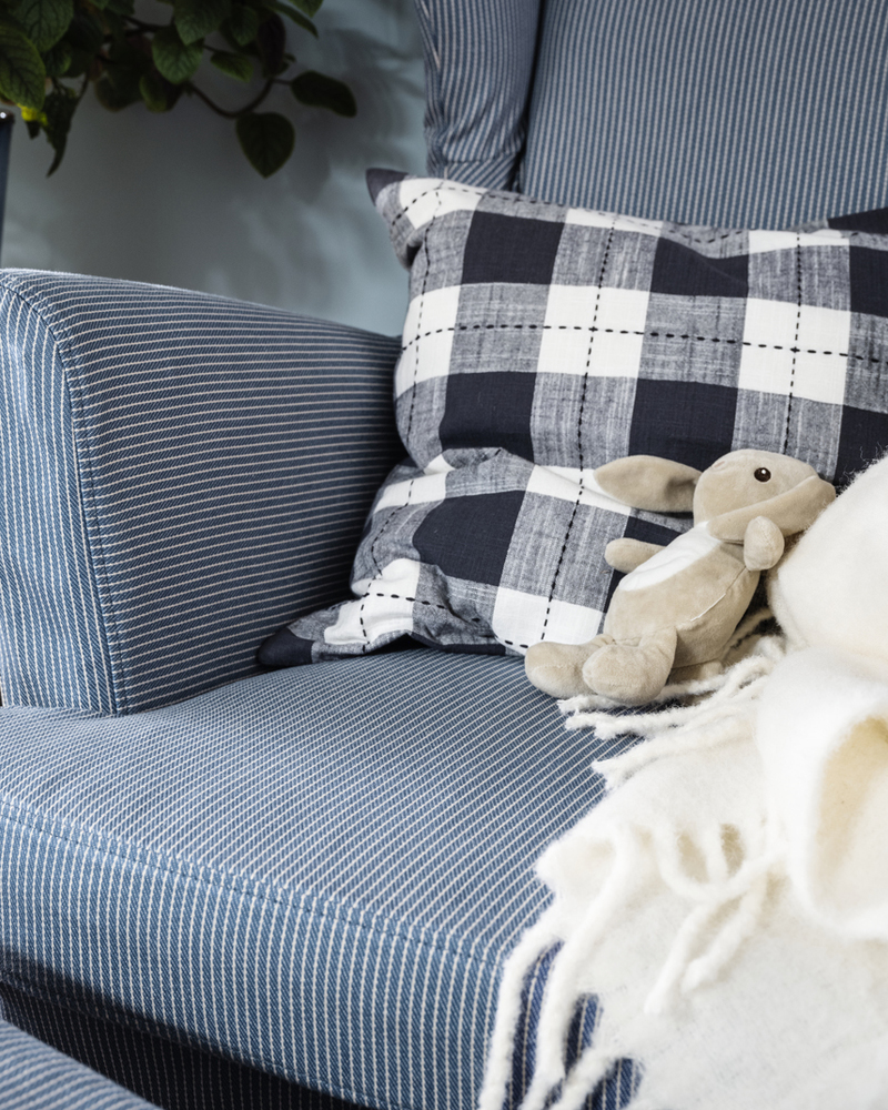 A toy rabbit lies against a cushion on a STRANDMON wing chair with a slipcover with a dark blue/beige stripe pattern.