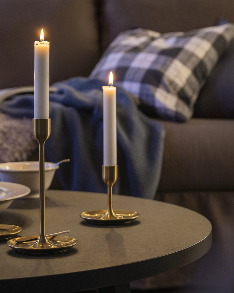 Three FULLTALIG candlesticks with lit candles stand on a dark brown STOCKHOLM 2025 coffee table near a HYLTARP sofa.