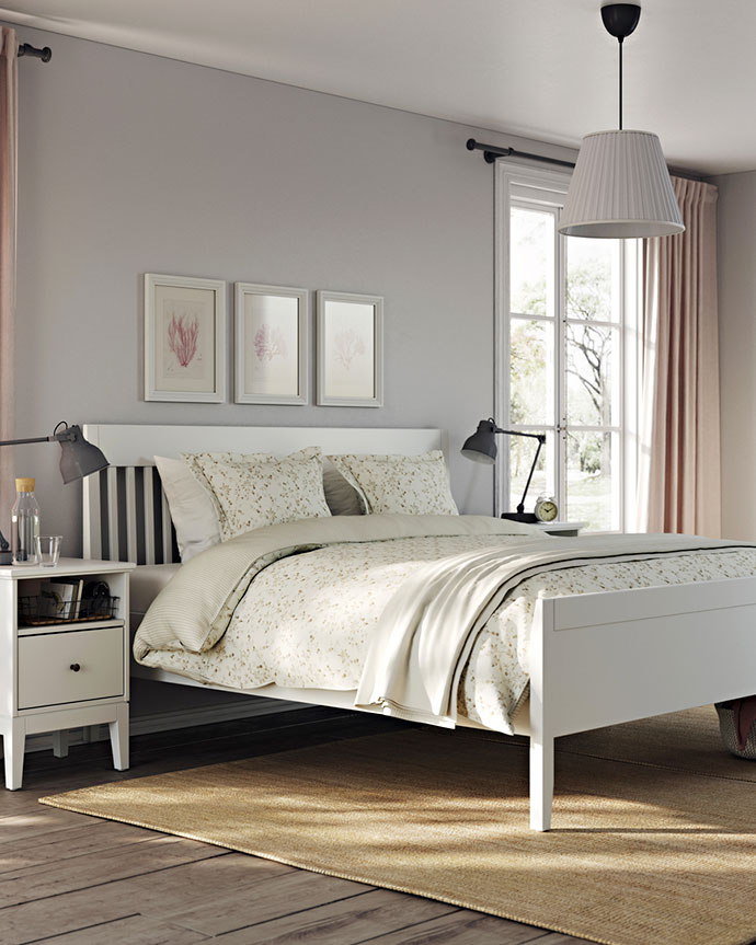 Dormitorio tranquilo y luminoso con cama blanca, ropa de cama floral, alfombra de yute y cortinas rosadas. Ventana grande y arte de pared.
