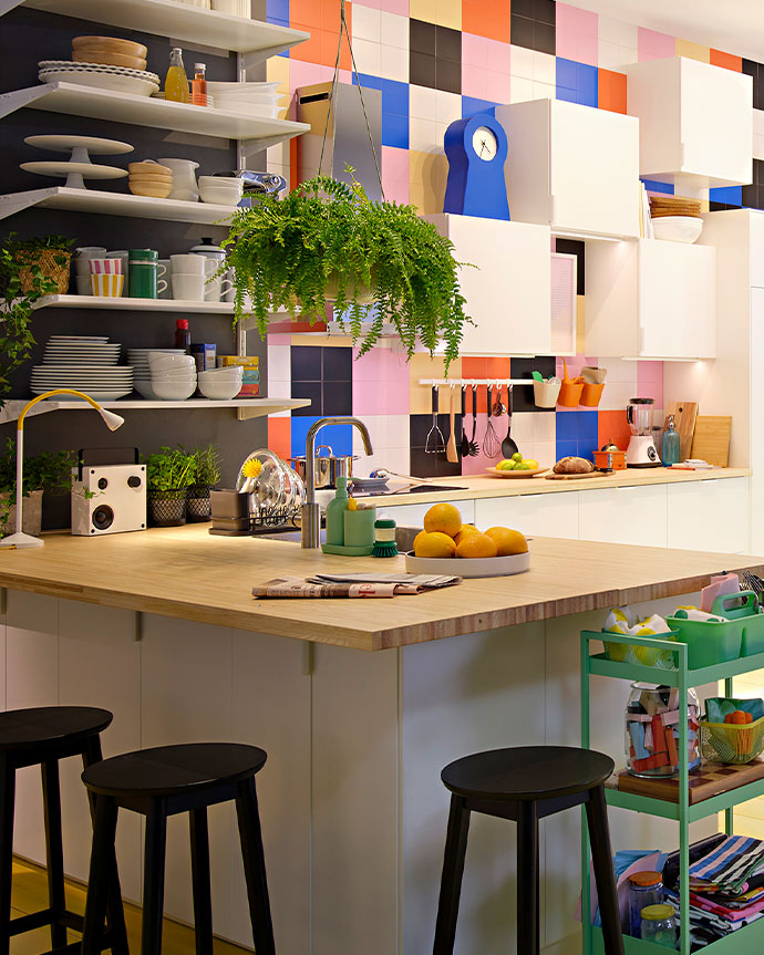 Cocina moderna con isla de madera clara, estantes abiertos, y un salpicadero de azulejos en bloques de colores vivos y negro.