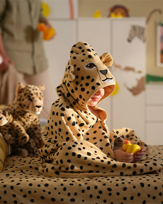 Niño con disfraz de leopardo jugando en dormitorio con ropa de cama a juego y peluches