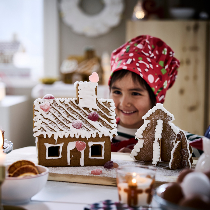 Niña decorando una casa y un árbol de jengibre con glaseado blanco, caramelos y azúcar glas.