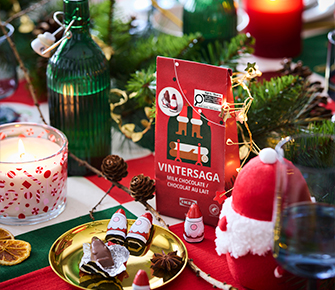 Barra de chocolate con leche VINTERSAGA y bombones con forma de Papá Noel sobre un plato dorado en una mesa festiva.