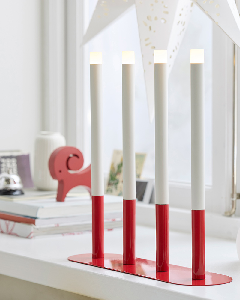 Una vela LED STRÅLA con base roja, acompañada de libros y una decoración VINTERFINT.