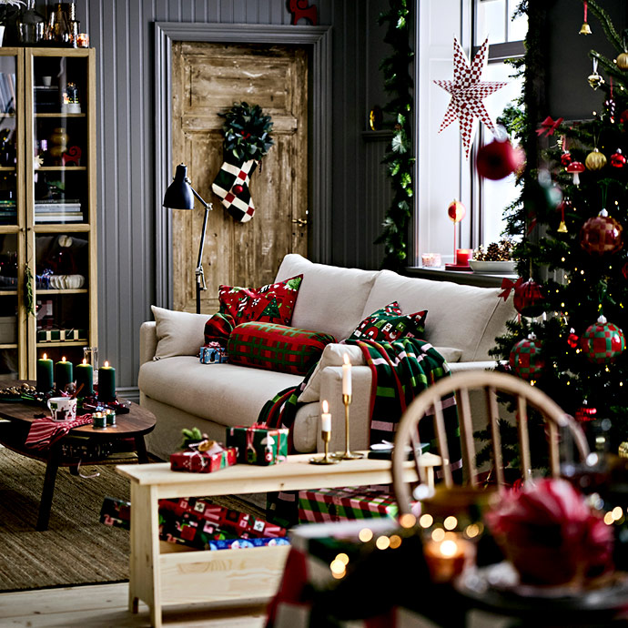 Sala de estar con sofá, árbol de Navidad grande y vitrina, decorada con textiles de cuadros rojos y verdes para fiestas.