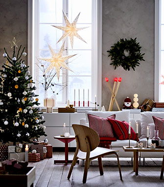 Sala decorada para Navidad, con árbol, dos estrellas luminosas en la ventana y un sofá blanco con cojines a rayas rojas.