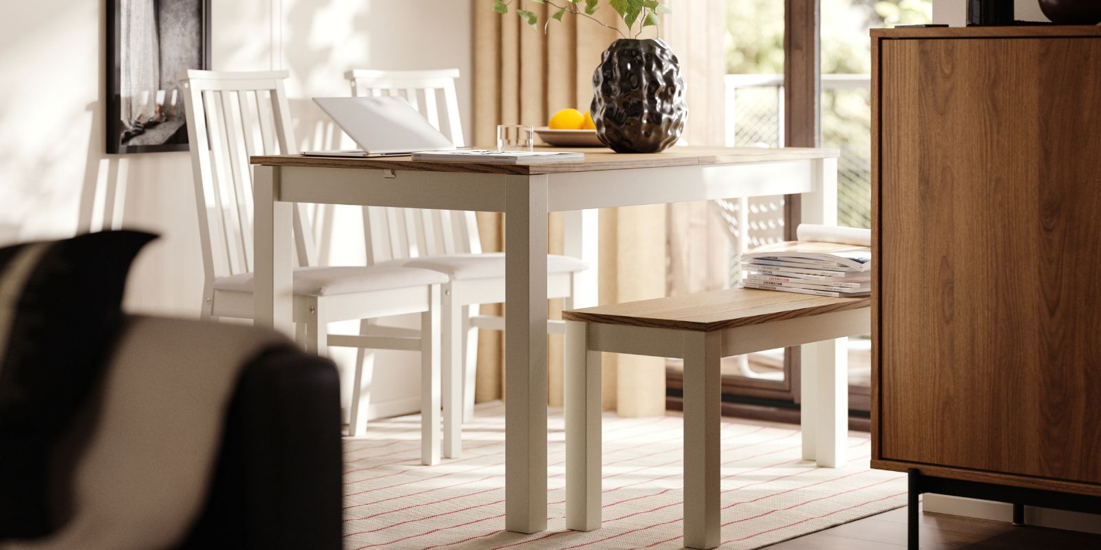 Un área de comedor tiene una mesa extensible ÅLHULT de color beige/marrón con un banco a un lado y dos sillas con asientos blandos al otro.