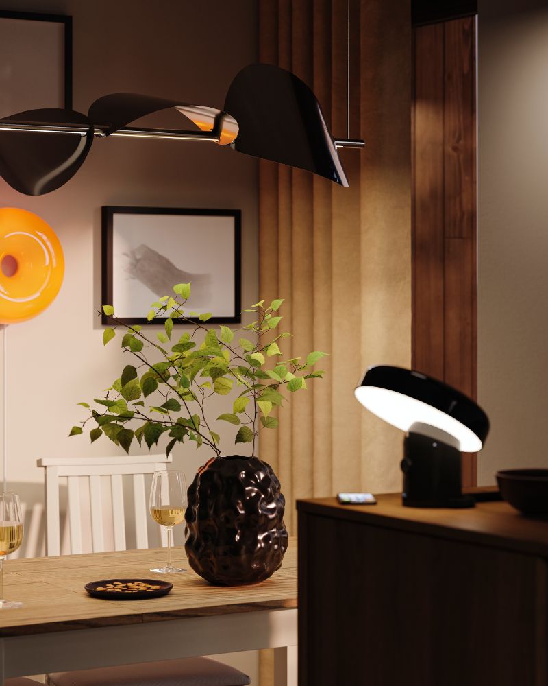 Un jarrón STOCKHOLM negro está apoyado sobre una mesa en un acogedor comedor con varias lámparas, lo que crea una atmósfera suave.