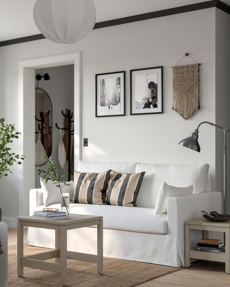 Un sofá HYLTARP de dos plazas, con dos cojines adicionales, se encuentra junto a una pared, cerca de un conjunto de dos mesas nido HAVSTA.