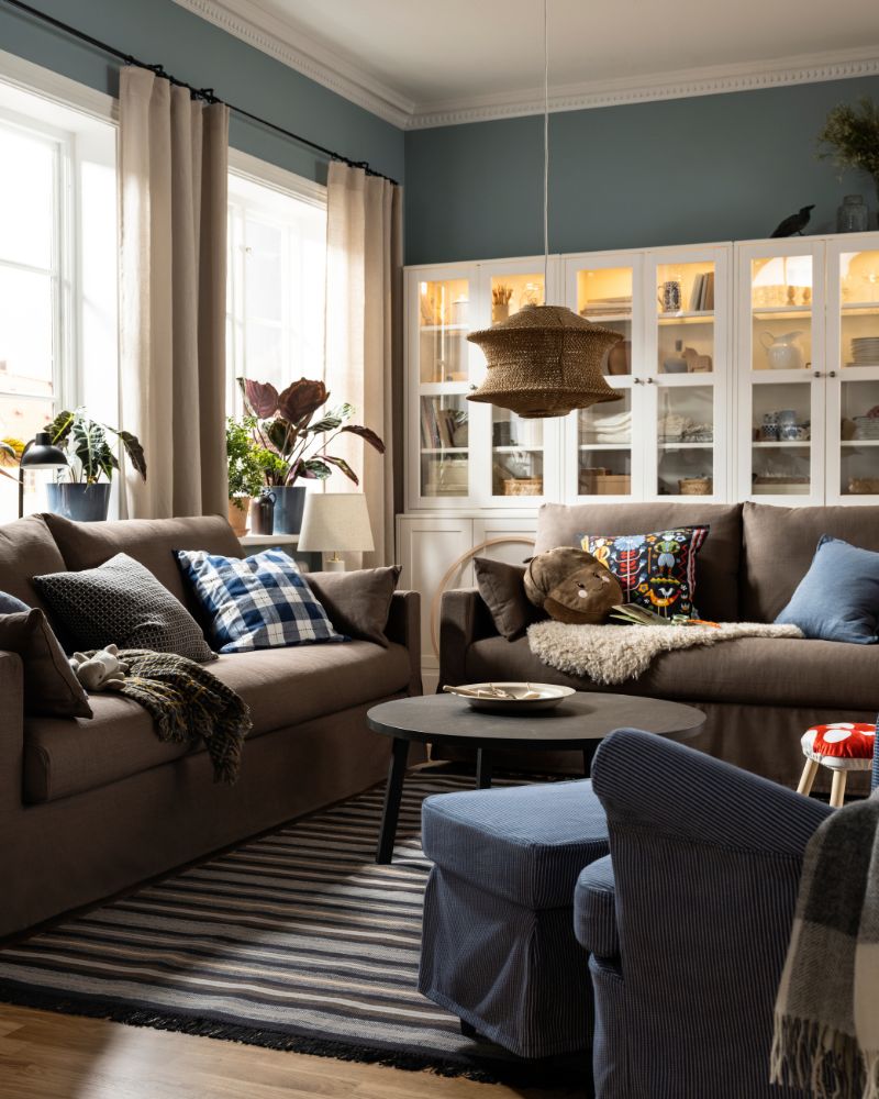 Dos sofás HYLTARP con muchos cojines adicionales se encuentran cerca de una mesa de centro STOCKHOLM 2025 de color marrón oscuro sobre una alfombra RÅVAROR.