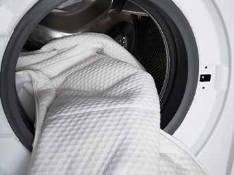 White bedding being loaded into washing machine drum for easy home laundry care
