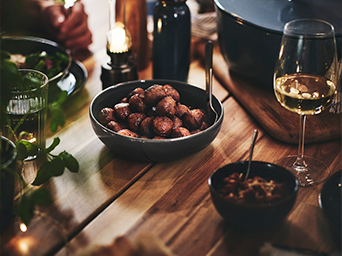 Mesa de comedor acogedora con albóndigas en cuenco oscuro, copa de vino blanco y botellas sobre madera