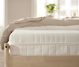 Primer plano de un colchón de espuma con textura acolchada, colocado sobre una base de cama de madera clara.