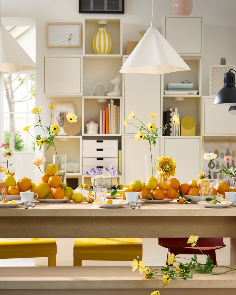 Una mesa BERGSHYTTAN tiene una decoración con platos blancos y vasos POKAL, además de naranjas y limones decorativos sobre los platos.