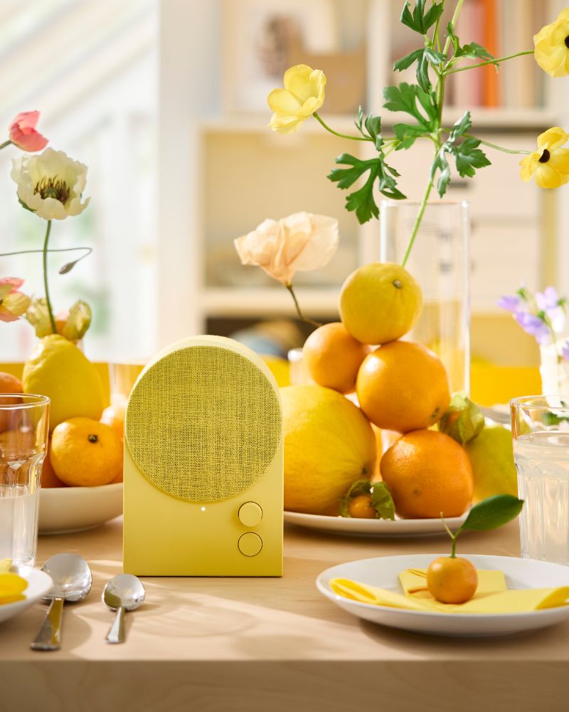 Un altavoz Bluetooth NATTBAD amarillo está colocado sobre una mesa decorada en tonos amarillos y naranjas para una fiesta festiva.