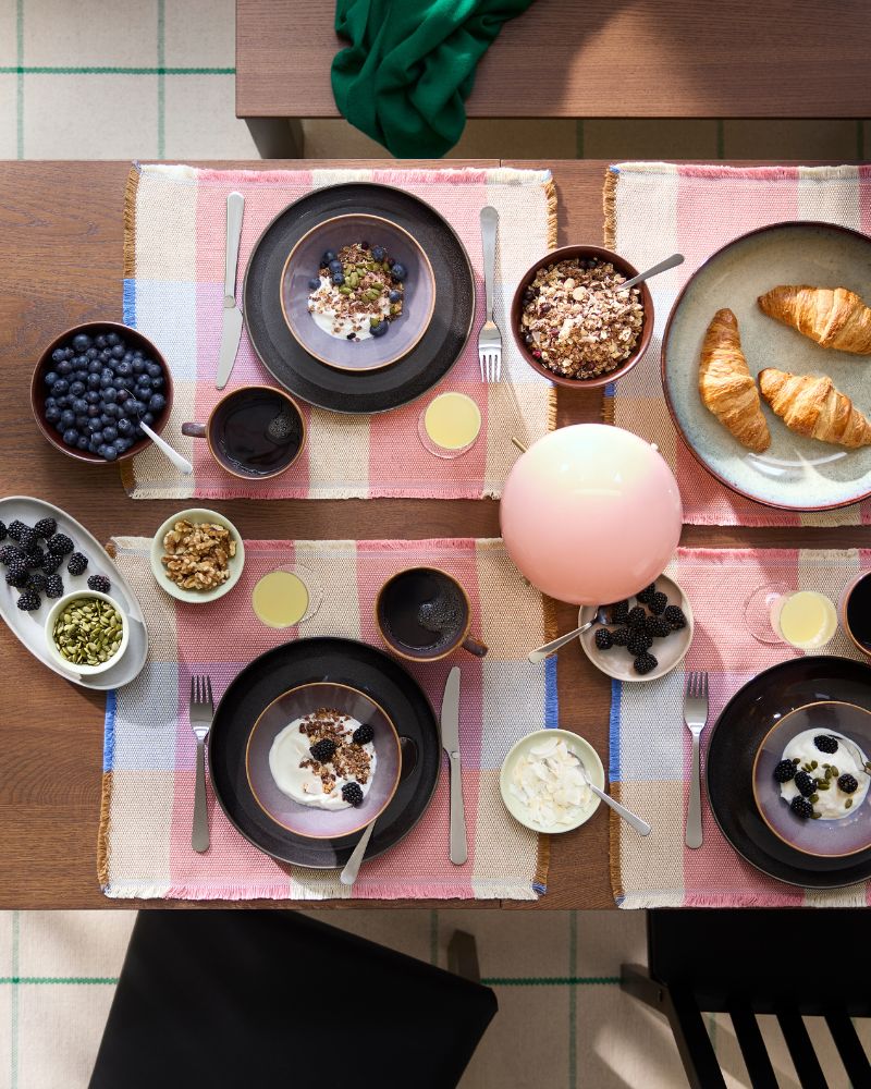 Una vista de águila de una mesa extensible ÅLHULT en color negro/marrón muestra un banco y sillas alrededor, y está preparada para un brunch.