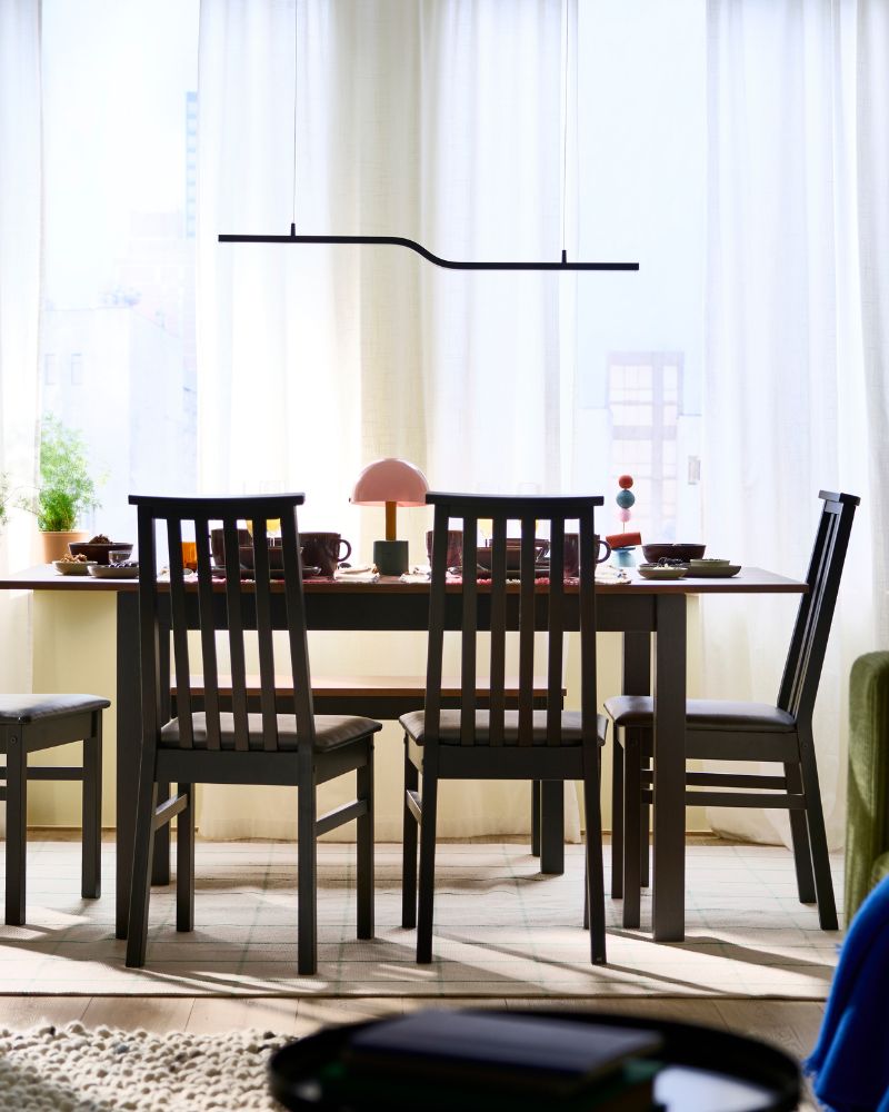 Un comedor con una mesa extensible ÅLHULT rodeada por cuatro sillas y realzada por una lámpara colgante LED PILSKOTT.