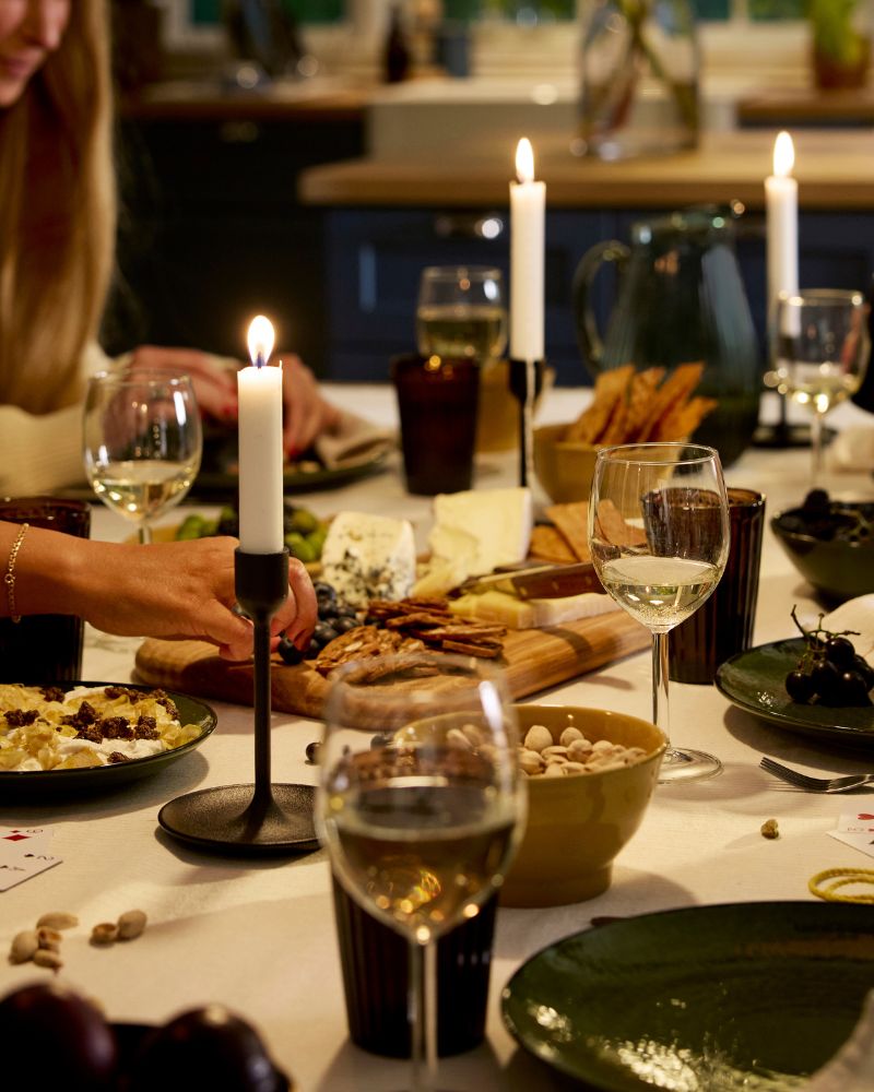 Las personas están jugando cartas en una mesa festiva con candelabros, copas de vino y platos con queso y galletas saladas.