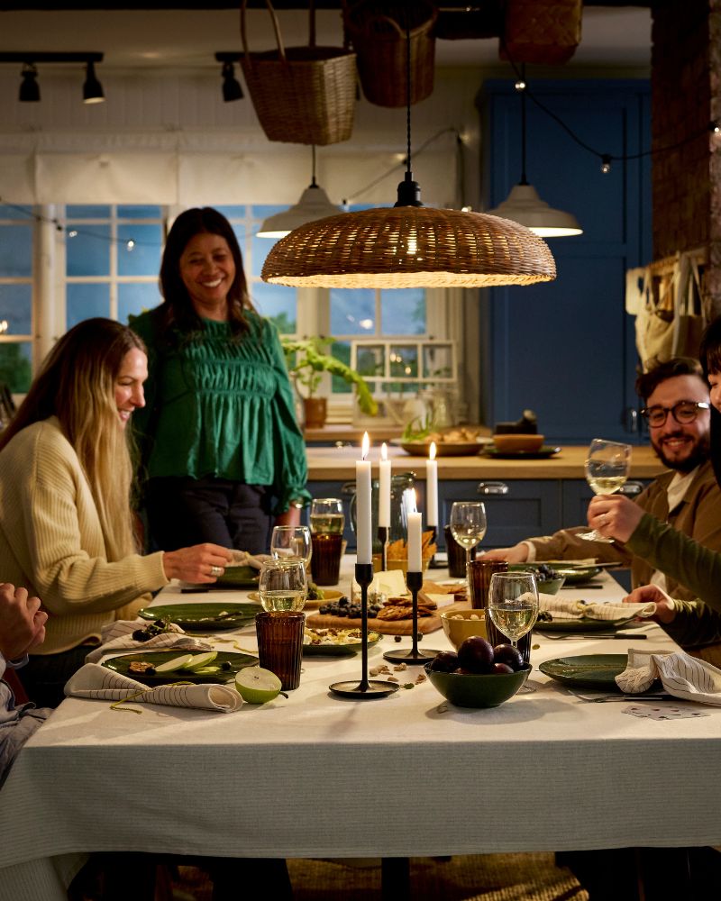 Las personas están reunidas alrededor de una mesa para disfrutar de una comida de queso y fruta fresca, todo en un ambiente acogedor iluminado con velas.