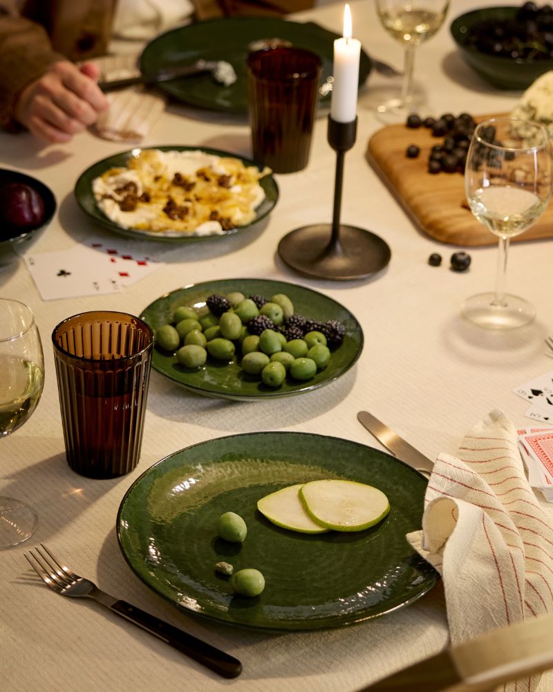Las personas están sentadas alrededor de una mesa festiva decorada con copas de vino y platos, cuencos y platos pequeños verdes de la línea PELARKAKTUS.