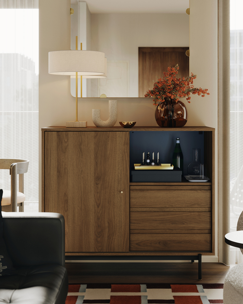 Una lámpara de mesa STOCKHOLM 2025 y un jarrón STOCKHOLM 2025 se encuentran sobre un armario RÅDMANSJÖ en una sala de estar digna de Instagram.