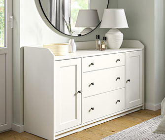 Cómoda/aparador blanco de estilo clásico con tres cajones centrales y dos armarios laterales en un dormitorio.