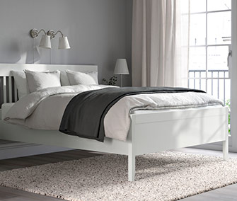 Dormitorio con cama doble blanca de estilo tradicional, ropa de cama blanca y manta gris, sobre una alfombra beige.