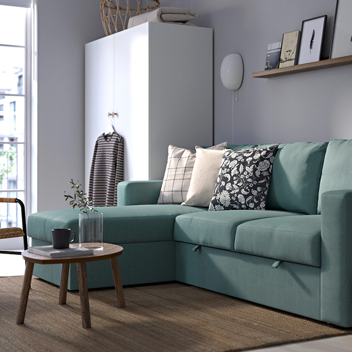 Sofá cama modular de esquina color turquesa claro con chaise longue, cojines estampados y una mesa auxiliar de madera.