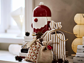 Tres pequeñas bolsas de tela festivas con patrones de rayas y puntos, junto a una figura roja y blanca de Santa Claus. Abeto de fondo.