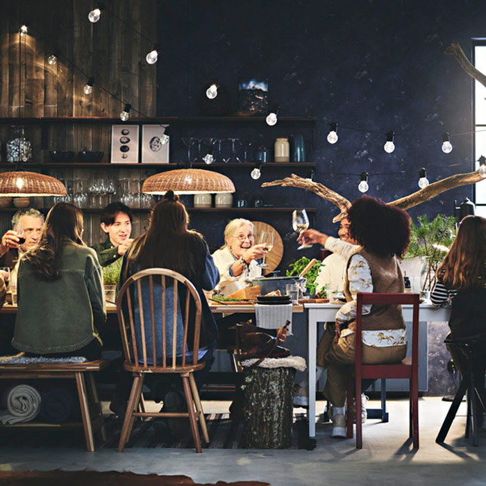 A family or group of friends sharing a festive meal in a rustic dining room with dark walls and string lights. Cozy atmosphere.