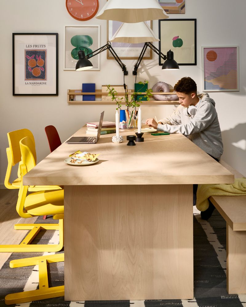A person is sitting on a BERGSHYTTAN bench at a BERGSHYTTAN table that’s placed against a picture wall.