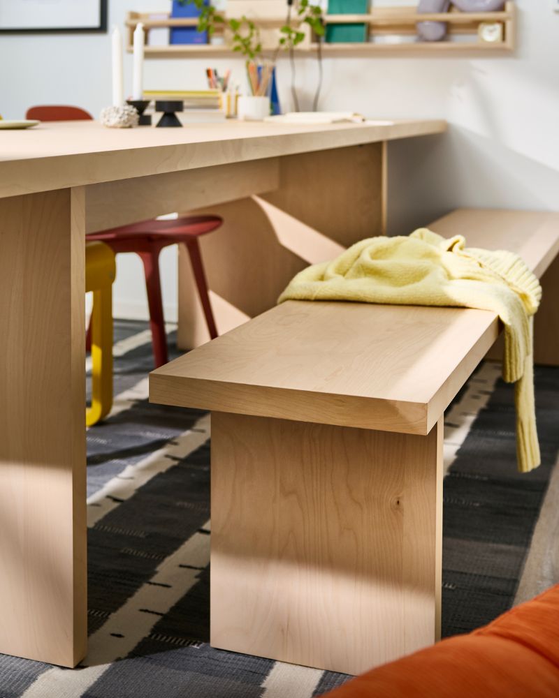 A BERGSHYTTAN bench in bright birch veneer is standing next to a large BERGSHYTTAN table in the same style and colour