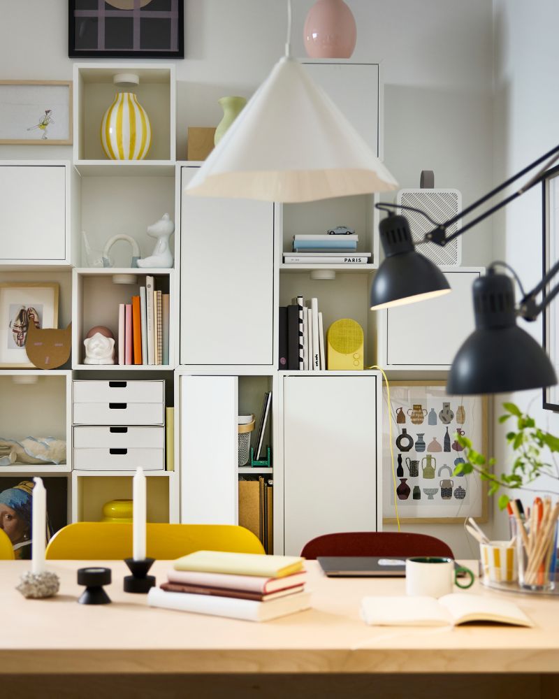 White EKET cabinets are mounted on a white wall behind a BERGSHYTTAN table, and there are things stored on the shelves.