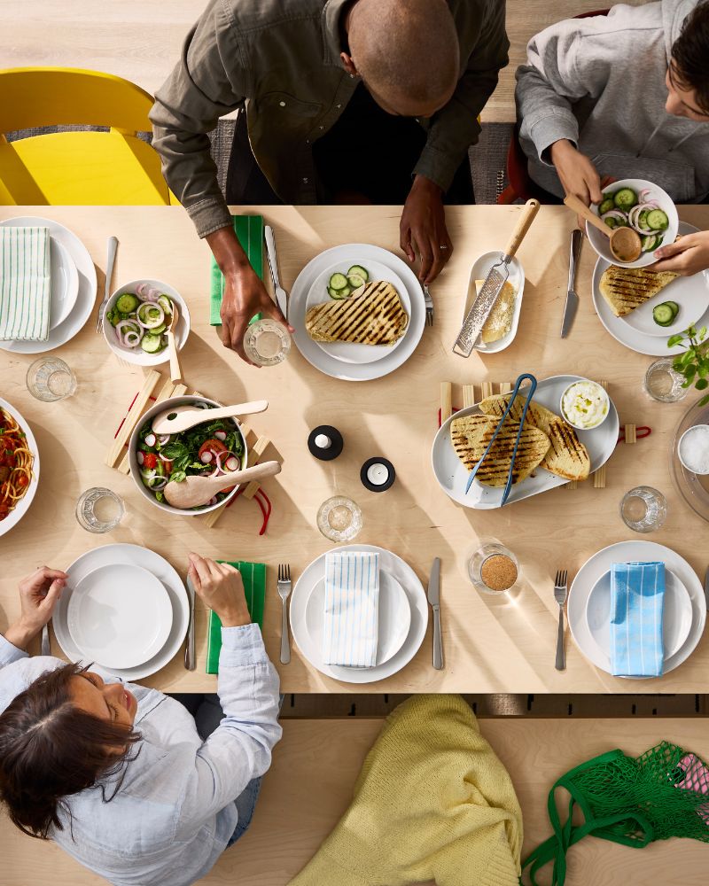 A bird’s-eye view of a BERGSHYTTAN table in birch veneer where people are sharing a meal together on white GODMIDDAG plates.