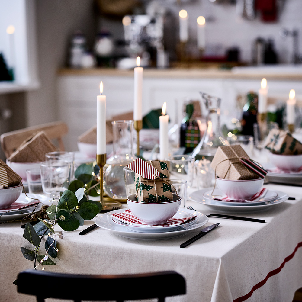 A table decorated for Christmas with VINTERFINT bowls, OFTAST plates, unscented JUBLA candles, STORSINT and STOCKHOLM 2025 decanters, and a VINTERFINT tablecloth.