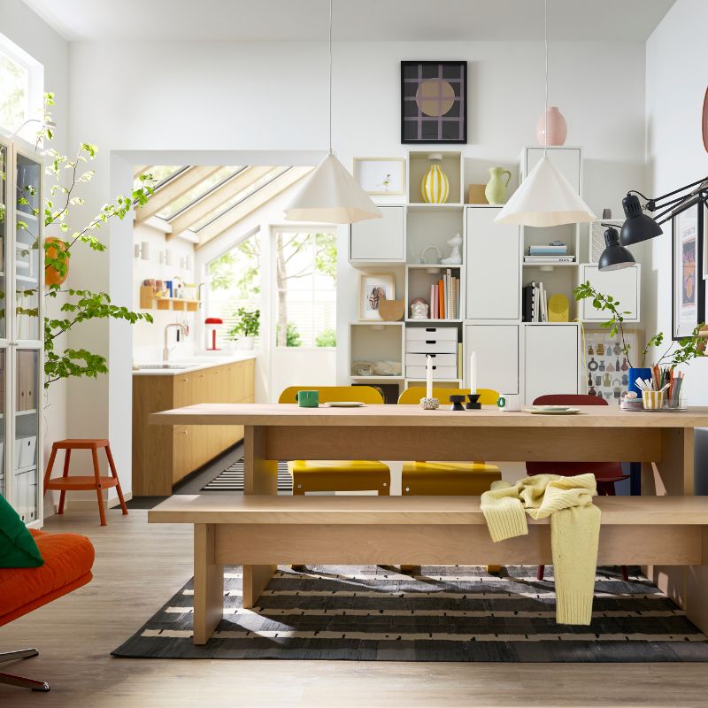 A bright dining room has a BERGSHYTTAN table with a bench in birch veneer on one side and colourful chairs on the other.