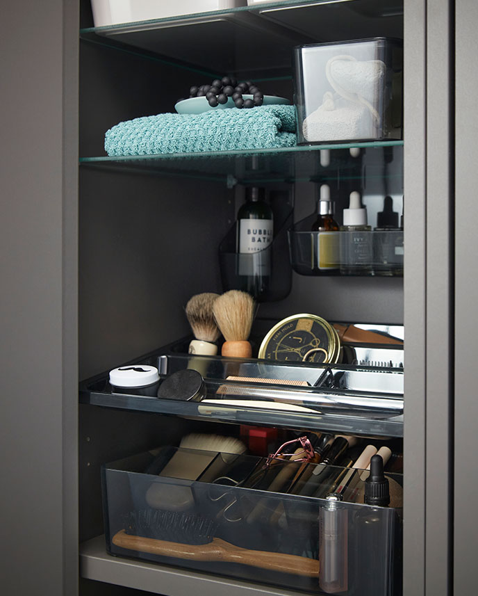  Close-up inside a dark grey HAVBÄCK high cabinet with  door, displaying neatly arranged toiletries and  grooming items.
