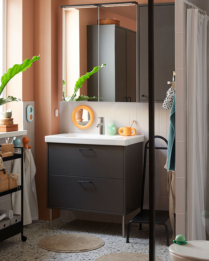 Tiled bathroom setting with a black NISSAFORS trolley  with storage boxes, accessories, toiletries, next to a  step stool.