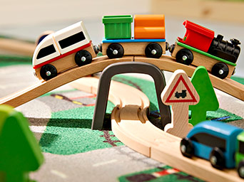 Tren de juguete de madera con vagones y locomotora sobre una vía elevada y un puente, rodeado de árboles de madera.