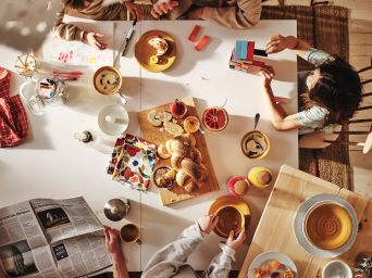 A family of five, viewed from above enjoying a leisurely breakfast around their large white dining table.